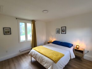 Quarto com cama, janela, duas luminárias de cabeceira e duas fotos emolduradas na parede.