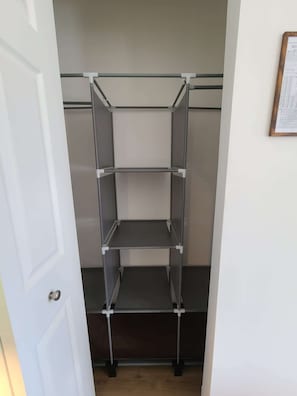 Una estructura metàl·lica d'estanteries amb tres nivells, una porta blanca i un document emmarcat a la paret.