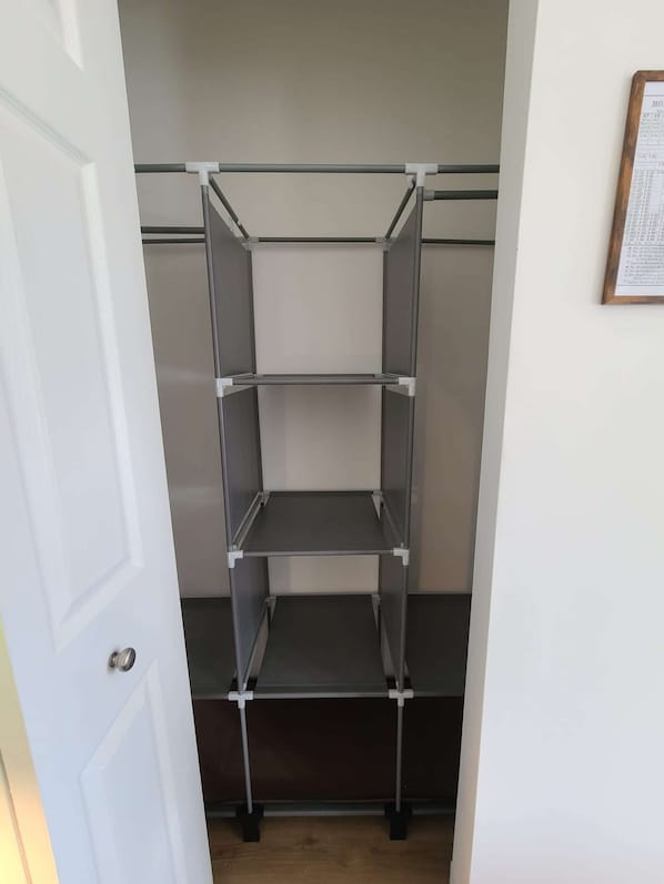 A metal shelving unit with three shelves, a white door, and a framed document on the wall.