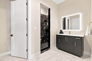 Ein Badezimmer mit einer weißen Tür, einer Dusche mit Marmorwand und einem dunklen Schrank mit Spiegel.
