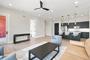 A modern living room with a sofa, a coffee table, and a dining area with chairs and a kitchen in the background. - Unit 7 - The Steeplechase · 2 Bed · 2 Bath (Owensboro)