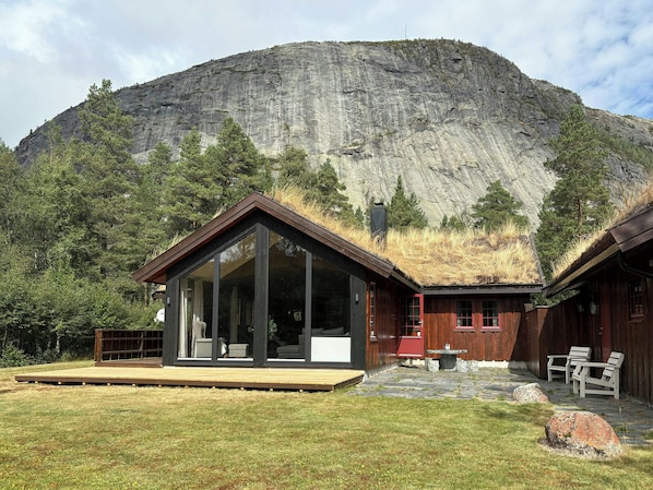 A modern cabin with large windows, a wooden deck, and a thatched roof.