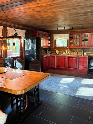 A kitchen with wooden cabinets, a black refrigerator, and a dining table with chairs. - Cabin by Løfjell with ski tracks from the door (Agder)