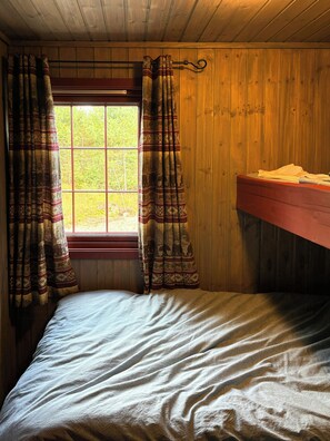 Quarto com cama, janela com cortinas e parede de madeira.