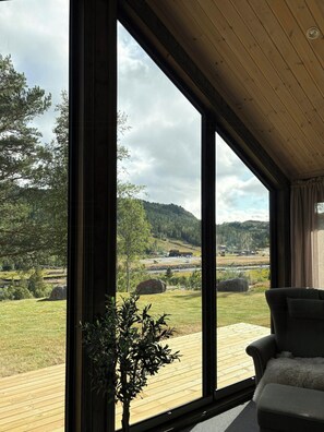 A room with large windows, a wooden ceiling, and a view of a green landscape with hills. - Cabin by Løfjell with ski tracks from the door (Agder)