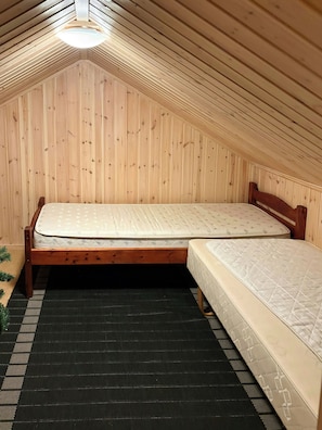 A room with a sloped ceiling, wooden walls, a bed with a mattress, and a black and white patterned rug.