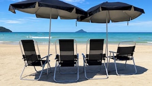 Ein Strand mit drei Liegen und zwei Sonnenschirmen.