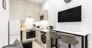 Ett modernt kök med inbyggd ugn, mikrovågsugn och diskmaskin, en matplats med bord och stolar samt en platt-TV som är monterad på väggen.