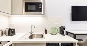 A modern kitchen with a stainless steel microwave, a toaster, a sink, a kettle, and a coffee maker. - South Kensington Base Near Hyde Park (London)