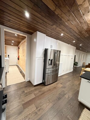 A modern kitchen with white cabinetry, a stainless steel refrigerator, and wooden flooring. - The Midpoint Manor (Central)