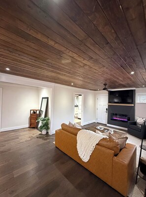 A modern living room with a wooden ceiling, a brown sofa, a flat-screen TV, and a fireplace.