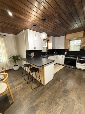 A modern kitchen with a wooden ceiling, white cabinets, a central island with stools, and stainless steel appliances.