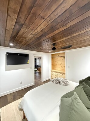 A bedroom with a bed, a television mounted on the wall, and a wooden ceiling. - The Midpoint Manor (Central)