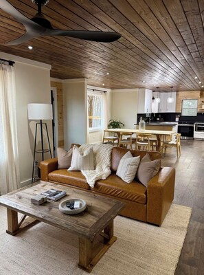 A cozy living room with a brown leather sofa, a wooden coffee table, and a ceiling fan. - The Midpoint Manor (Central)