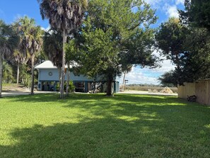 A residential property with a well-maintained lawn, a house with a porch, and a large tree providing shade. - 3-bedroom stilt home designed for hunters, fisherman, scallopers & nature lovers (Crystal River)
