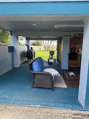 An outdoor covered patio with a wicker sofa, a grill, and a wooden chest.