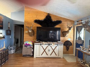A room with a mounted deer head, a large flat-screen TV, and a rustic wooden wall. - 3-bedroom stilt home designed for hunters, fisherman, scallopers & nature lovers (Crystal River)