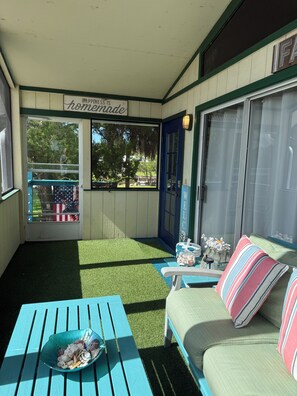 A porch with a green artificial turf, a blue door, a bench, a table, and a couch with striped pillows. - 3-bedroom stilt home designed for hunters, fisherman, scallopers & nature lovers (Crystal River)