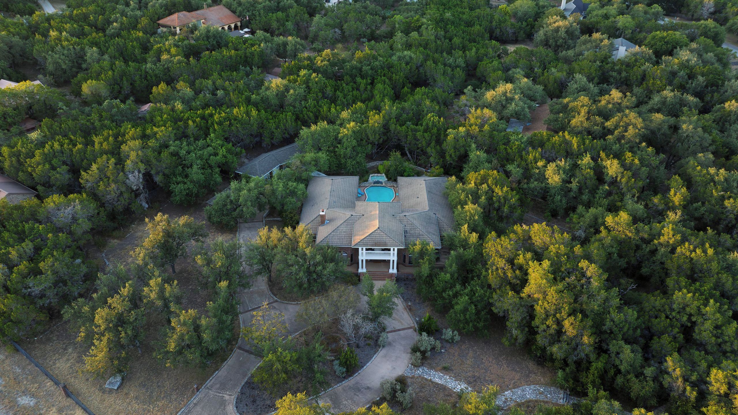 Una casa rodeada de árboles frondosos, con piscina y un porche cubierto.