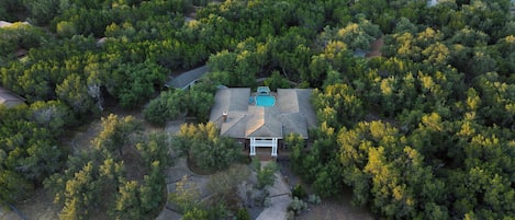 Una casa rodeada de árboles frondosos, con piscina y un porche cubierto.