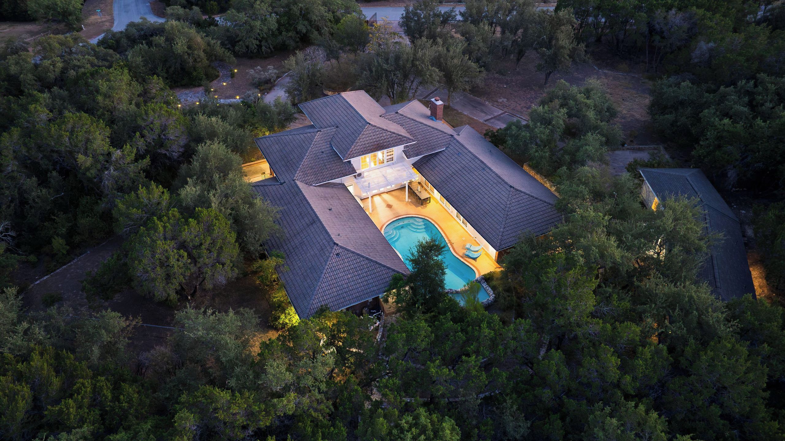 Ein Wohnhaus mit Swimmingpool, mehreren Dachabschnitten und dichter Baumumgebung.