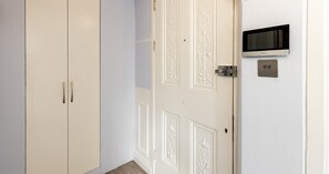 Een kamer met een witte inbouwkast, een deur met decoratieve panelen, een aan de muur bevestigde televisie en een thermostaat.