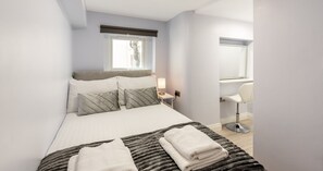 A bedroom with a bed, bedside lamp, and a chair. - South Kensington Base Near Chelsea (London)
