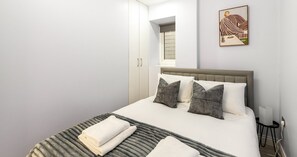 Een hotelkamer met een bed, kussens, een nachtkastje, een lamp en een schilderij aan de muur.