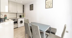 A modern kitchen with white cabinets, a washing machine, and a dining area with a table and chairs. - South Kensington Base Near Chelsea (London)