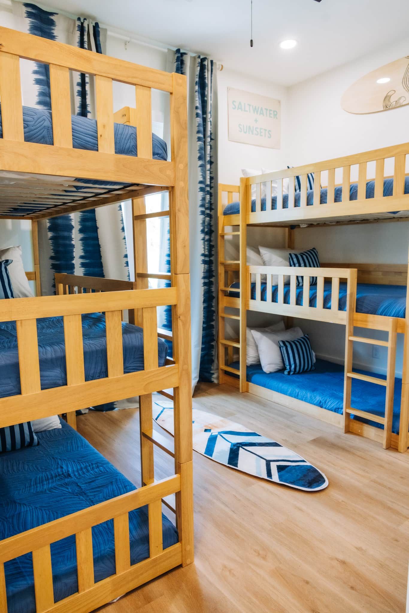 Een kamer met stapelbedden, een surfplank en een bord waarop 'SALTWATER SUNSETS' staat.