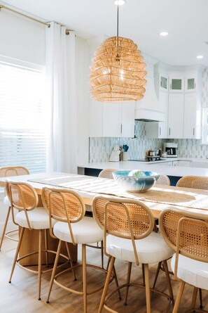 A modern kitchen with white cabinets, a central island with a bowl, and a hanging rattan light fixture. - The Cove & Beach Nook | Sleeps 16 | Spa · Theater (Walton County)