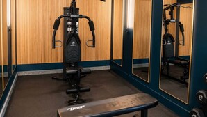 Een sportschool met een multifunctionele fitnessapparaat, een bank en spiegels aan de wanden.