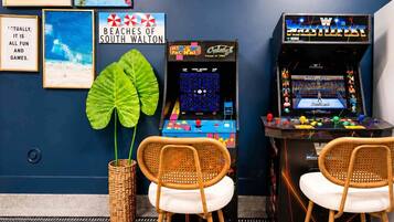Ein Zimmer mit zwei Spielautomaten, einer großen Pflanze und zwei Korbstühlen.