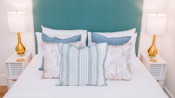 Una cama con cabecera color turquesa, ropa de cama blanca y dos lámparas de noche con bases doradas.