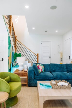 A modern living room with a blue sofa, a green armchair, and a wooden coffee table. - The Cove | 4BR · 12 Guests | Spa · Theater · Gym (Walton County)
