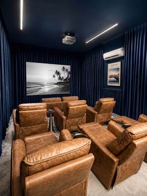 Ein Heimkino mit Ledersessel, großem Flachbildfernseher und Projektor an der Decke.