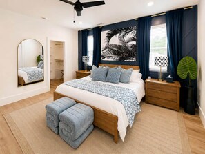 A bedroom with a bed, bedside tables, a mirror, a ceiling fan, and a large window with curtains. - The Cove | 4BR · 12 Guests | Spa · Theater · Gym (Walton County)
