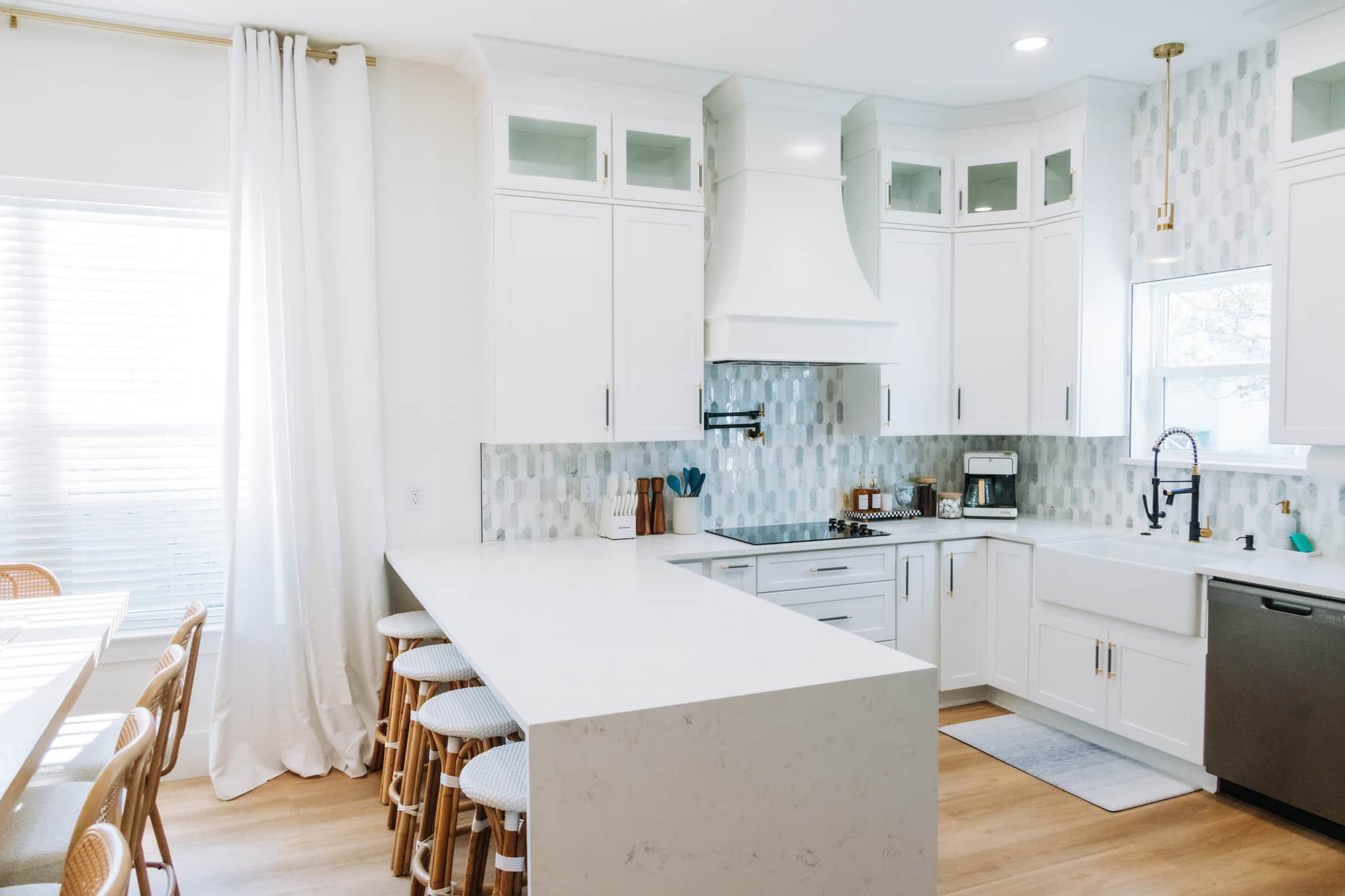 Una cocina moderna con armarios blancos, una isla central y un comedor con sillas de mimbre.
