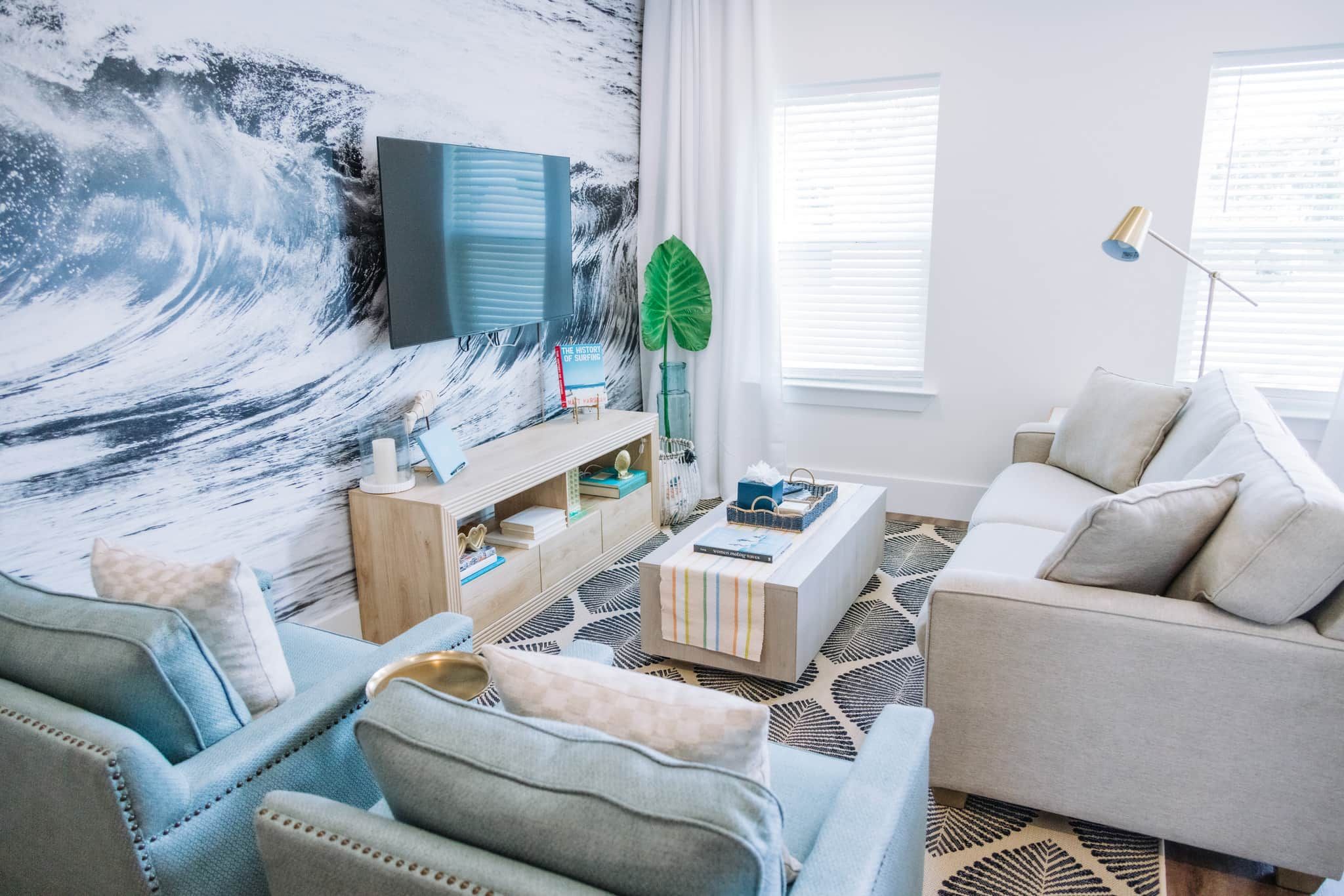 A modern living room with a large wave mural, a flat-screen TV, a coffee table, sofas, and a patterned rug.