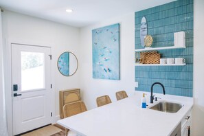 A modern kitchen with a white countertop, a sink, and a blue tiled backsplash. - The Surf Shack @ The Cove | 2BR · 6 Guests | Gym · Games (Walton County)