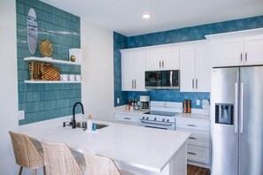 A modern kitchen with white cabinets, a stainless steel refrigerator, and a blue backsplash. - The Surf Shack @ The Cove | 2BR · 6 Guests | Gym · Games (Walton County)
