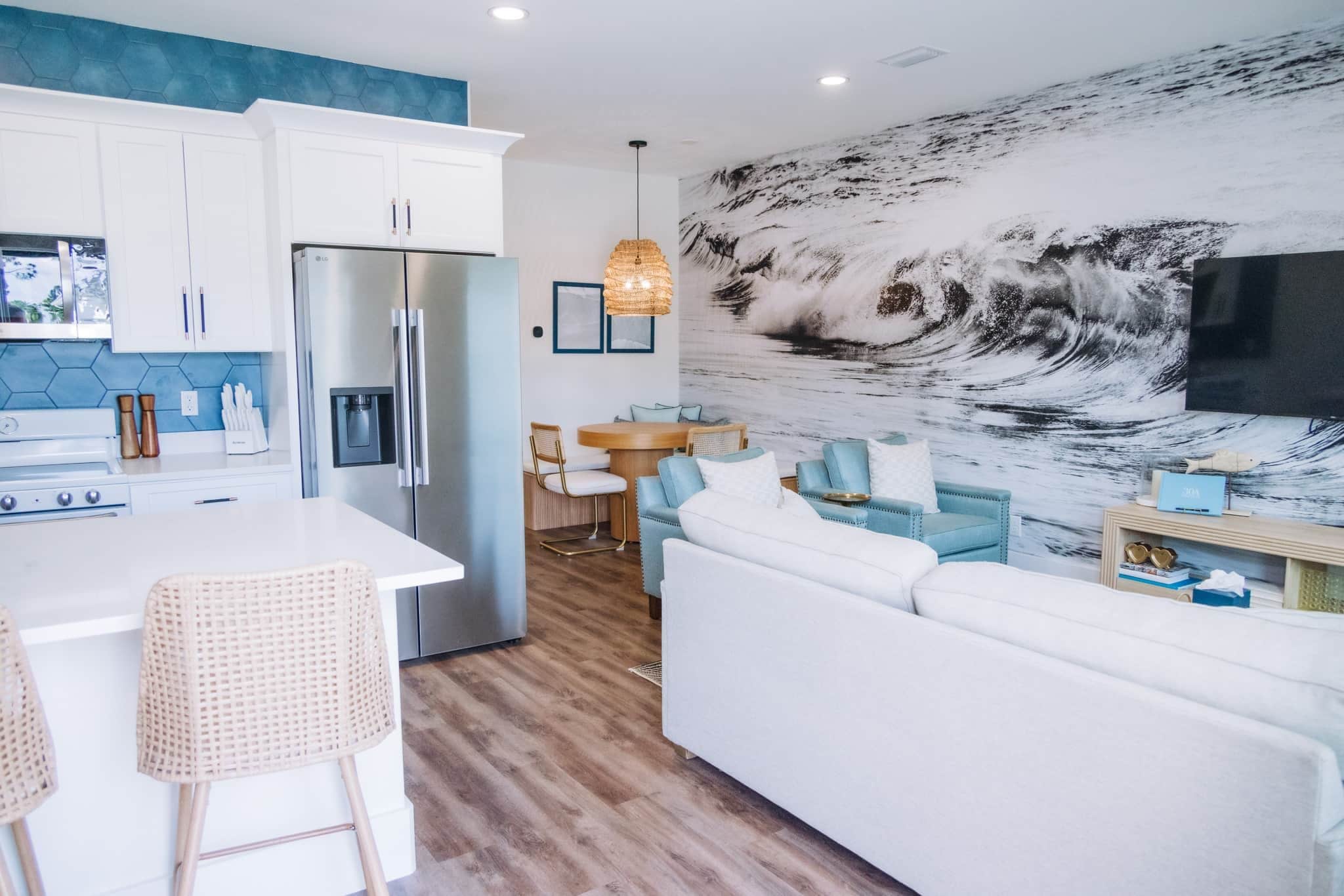 A modern kitchen with white cabinets, a stainless steel refrigerator, and a dining area with a round table and blue chairs.