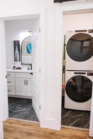 A laundry room with a front-loading washer and dryer, a sink, and a mirror. - The Surf Shack @ The Cove | 2BR · 6 Guests | Gym · Games (Walton County)