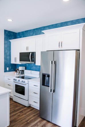A modern kitchen with white cabinets, a stainless steel refrigerator, a microwave, and a stove. - The Surf Shack @ The Cove | 2BR · 6 Guests | Gym · Games (Walton County)