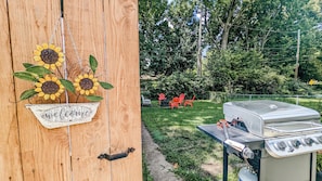 A wooden sign with sunflowers and a 'welcome' message, a barbecue grill, and outdoor seating with red chairs. - Beautiful 4-bedroom house in Springfield perfect for your getaway (Springfield)