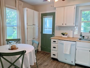 A kitchen with white cabinets, a green door, a dining table with a chair, and a window with blinds. - Beautiful 4-bedroom house in Springfield perfect for your getaway (Springfield)