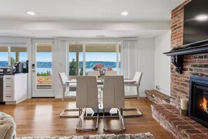 A modern kitchen with a brick fireplace, a dining area with a view, and a white interior. - Cascade & Sammamish: 180° Mountain & Lake Views (Bellevue)