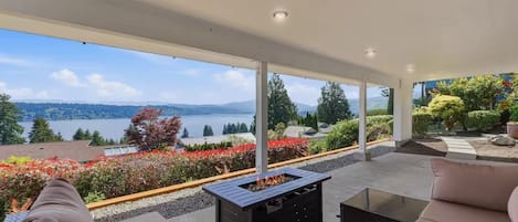 Un espacio de estar al aire libre cubierto con una chimenea, con vistas a un lago y colinas.