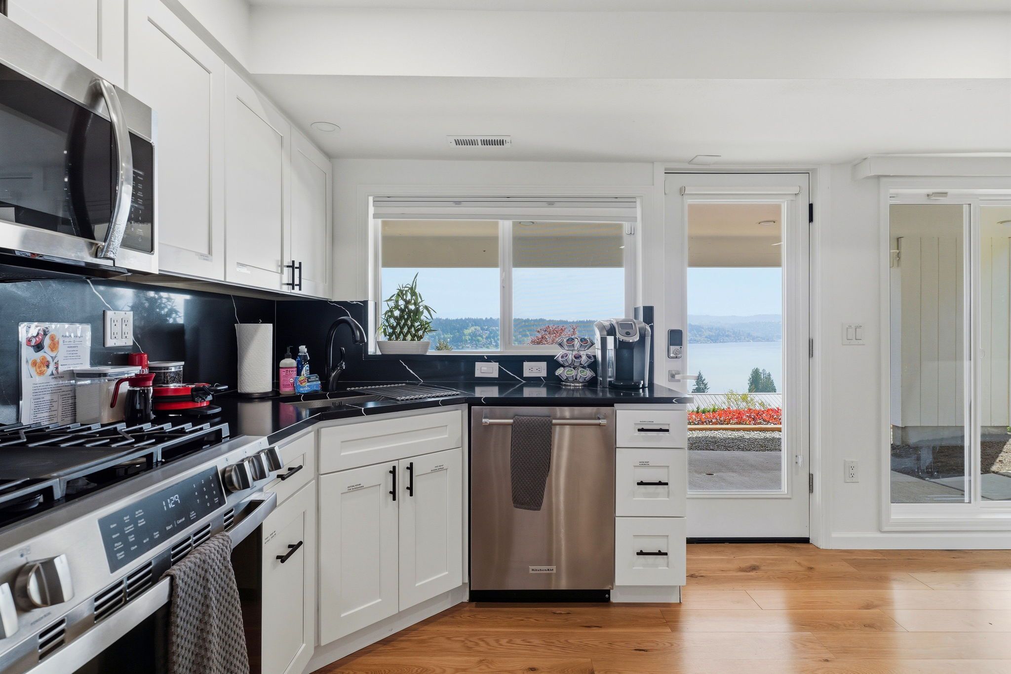 A modern kitchen with a stove, microwave, and dishwasher, large windows with a view, and a wooden floor.