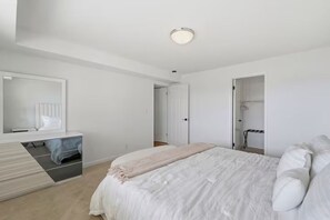 A bedroom with a bed, a bedside table, a mirror, and a walk-in closet. - Cascade & Sammamish: 180° Mountain & Lake Views (Bellevue)